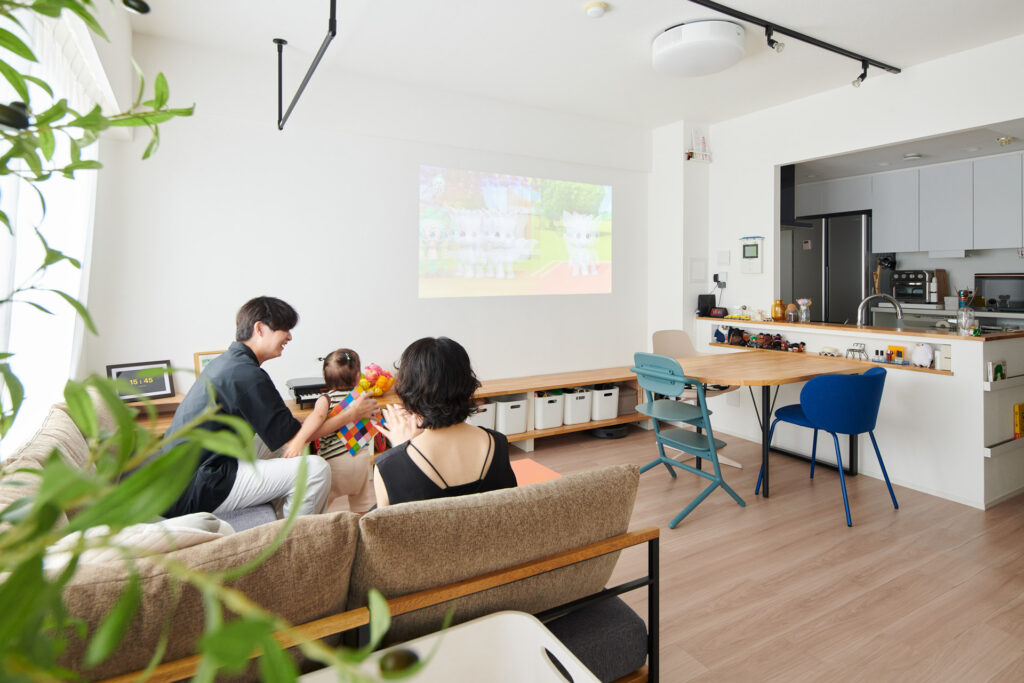 リビングでプロジェクターを楽しむ家族。壁面に映像が投影されている